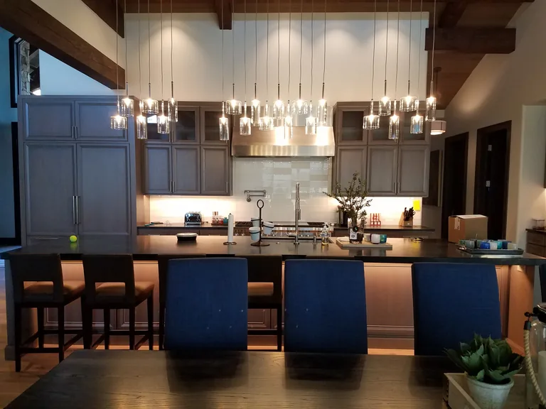 Large custom kitchen in Coeur d'Alene with a row of glass pendant lights over the island, dark cabinets and exposed timber beams