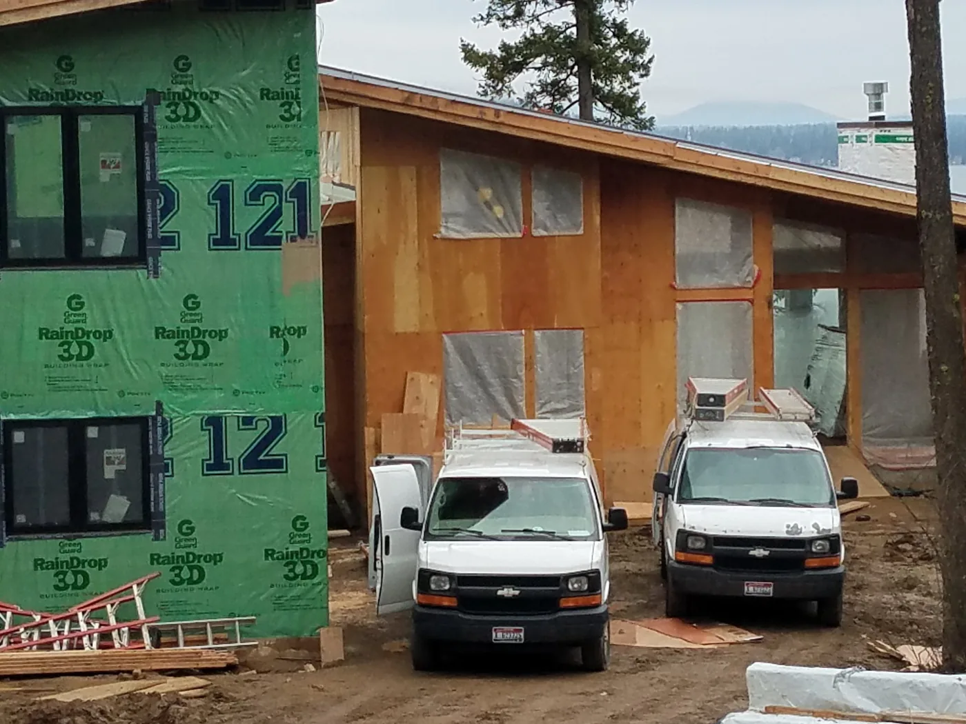 Two Northwest Wattage vans parked outside a house under construction during the electrical rough-in stage